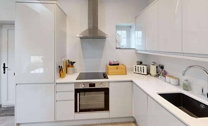 A modern, white gloss kitchen with integrated appliances, hob, and sleek worktops.
